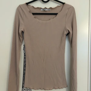 Beige ribbad långärmad topp från NA-KD - Beige långärmad topp med ribbad struktur och vågig kant vid halsringning och nederkant från NA-KD i storlek XXS. 
