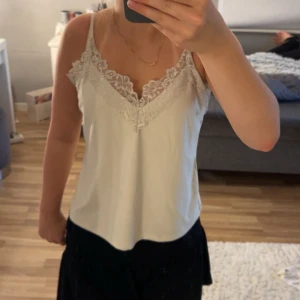 Vit spetslinnetopp från Vero Moda - Supersöt vit linnetopp från Vero Moda med tunna axelband och v-ringning dekorerad med romantisk spets. 