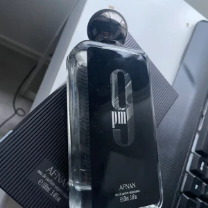 Afnan 9PM Eau de Parfum 100ml - Afnan 9PM Eau de Parfum i en stilren, rektangulär glasflaska med svart etikett och silverdetaljer. Flaskan har en rund, spegelblank svart kork som ger en lyxig känsla. Volymen är 100 ml och doften är känd för sina varma, kryddiga och söta toner. Har inte sprayat helt ny fick den för 2 dagar sedan 