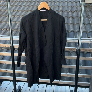Svart rock från Wera Stockholm - Säljer en svart lång rock från Wera Stockholm i storlek 34. Jackan har en avslappnad passform, långa ärmar och öppen front utan knäppning. Perfekt för dig som gillar minimalistisk och stilren look. Materialet känns lätt och smidigt.