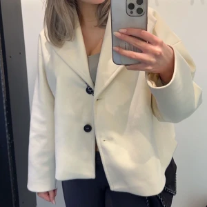 Oversized beige kappa  - Säljer en oversized beige kavajjacka med stora slag och två svarta knappar framtill. Jackan har lång ärm och rak passform, perfekt för en chill och trendig look. Materialet känns mjukt och ger en clean vibe till outfiten.