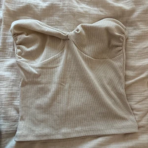 Beige ribbad tubtopp från Nelly - Säljer en beige ribbad tubtopp från Nelly i storlek S. Toppen har bandeau-modell med lätt twistad detalj framtill och är tillverkad i mjukt, stretchigt material. Perfekt för dig som gillar en clean och stilren look.
