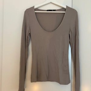 Beige långärmad topp från Lager 157 - Säljer en enkel och stilren beige långärmad topp från Lager 157. Modellen har en djup rundad ringning och är i ett mjukt bomullsmaterial. Perfekt att styla med jeans eller kjol för en clean look.