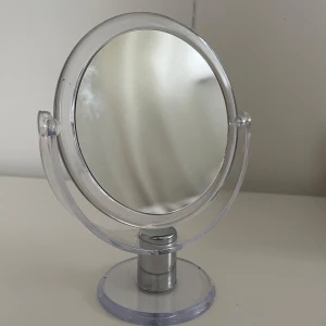 Rund sminkspegel med genomskinlig ram - Fint skick, måtten är: 18 cm på längden och ca 13 cm på diametern. En sida är vanlig spegel och andra är 5x inzoom. 360 graders vridning. (Första bilden visar 5x inzoomning från långt avstånd) Perfekt storlek för sminkbordet och enkel att flytta runt. (Köpt för 99kr) Torkar av den innan den postas!