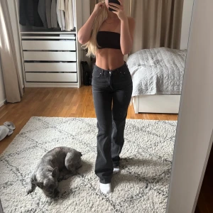 Svarta raka jeans med hög midja - Säljer ett par svarta jeans med hög midja och raka ben. Jeansen har klassisk femficksdesign, silverfärgade knappar och är i ett mjukt denimtyg. Snygg passform som sitter tajt över höfterna och släpper vid benen. Perfekta till crop tops eller hoodies.