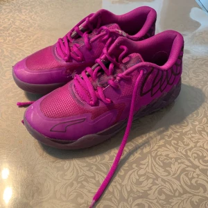 Puma MB.01 LaMelo Ball Lo Disco Basketskor rosa - Färgstarka Puma MB.01 Basketskor i samarbete med LaMelo Ball. Skorna är rosa med lila detaljer, har snörning och coola grafiska mönster på sidorna. Ovandelen är i syntet och mesh för bra andningsförmåga. Perfekta för dig som vill sticka ut med din stil.