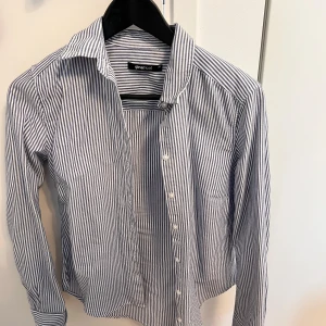 Randig skjorta från Gina Tricot - Snygg skjorta från Gina Tricot i vitt och blått med klassiskt randigt mönster. Skjortan har lång ärm, krage och knäppning framtill. Perfekt för en chill och stilren look. 