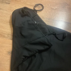 Svart  kostym omlottklänning med smala axelband - En svart kort kostymklänning från NA-KD med smala axelband och omlottdetalj. Klänningen har en figurnära passform och enkel, stilren design som ger en snygg siluett. Perfekt för dig som gillar minimalistisk stil och vill ha något klassiskt i garderoben.