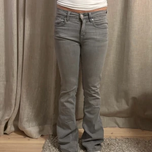 Grå bootcut jeans  - Snygga grå jeans från Gina i bootcut-modell. Jeansen har fem klassiska fickor, dragkedja och knapp framtill samt bälteshällor. Modellen är låg/mid waist och har en lätt utsvängd passform nertill. Perfekta till sneakers eller boots.