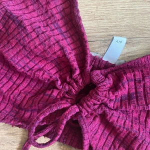 Vinröd ribbad bikiniöverdel med snörning - Vinröd bikiniöverdel med ribbat tyg och tunna axelband. Framsidan har snörning som kan justeras för en snygg passform. Modellen är croppad och har ett randigt mönster i mörkare nyans. Perfekt för stranden eller poolen!