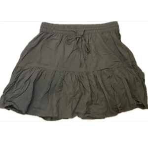 Olivgrön volangkjol från Pigalle - Kortkjol från Pigalle med volang och resår i midjan. Kjolen är olivgrön likast på bild 2 och har knytband framtill. Sval och fin och perfekt nu i sommar. 