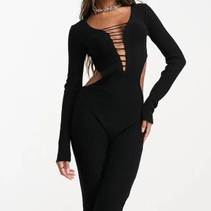 Svart ribbad jumpsuit med snörning - Svart ribbad jumpsuit tröja med djup v-ringning och cool snörningsdetalj framtill. Öppen rygg och framhäver midjan. Perfekt för dig som vill sticka ut med en edgy och trendig look.