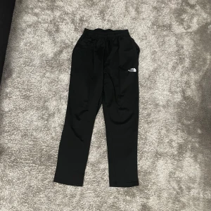 North face byxor - Svarta mjukisbyxor från The North Face med elastisk midja och logga tryckt på ena benet. Byxorna har en rak passform och är tillverkade i ett mjukt material som är skönt att ha på sig. Perfekta för chill eller träning.