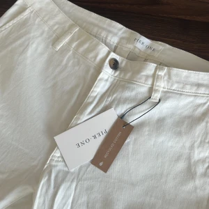 Vita chinos från Pier One, stl 33 - Snygga vita chinos från Pier One i storlek 33. Byxorna är tillverkade av återvunnen bomull och har klassisk rak passform med bälteshällor, sidfickor och bakficka. Perfekta för en clean och fräsch look. Lappen kvar, aldrig använda.