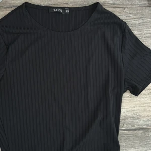 Svart ribbad topp från NLY One XS - En svart ribbad topp från NLY One i storlek XS. Toppen har korta ärmar och rund halsringning. 