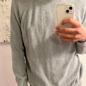 Grå stickad tröja från Zara - Säljer en stilren grå stickad tröja från Zara i storlek L. Tröjan har rund halsringning, ribbade muddar och är långärmad. Perfekt för lager-på-lager och passar till både jeans och chinos. Enkel och clean look som funkar året runt.