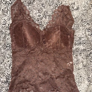 Brun spetslinne med v-ringning - Säljer ett brunt linne med v-ringning och breda axelband. Toppen är i spetsmaterial och har en croppad passform. Perfekt fest topp att styla till jeans eller kjol. Padding finns inuti så bh behövs inte. Lånade bilder 💕