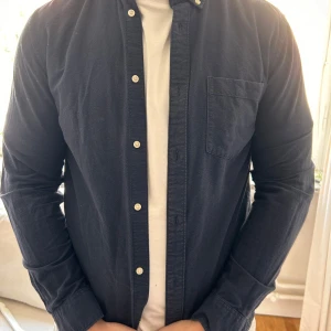 Mörkblå skjorta från H&M Regular Fit - Snygg mörkblå skjorta från H&M i regular fit. Skjortan har klassisk krage, vita knappar framtill och en bröstficka. . Långärmad modell som funkar året runt.