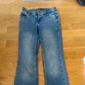 Blå bootcut jeans från Lee - Snygga blå jeans från Lee med klassisk bootcut-passform. Jeansen har fem fickor, bälteshällor och Lee-logga på bakfickan. De är tillverkade i mjukt denimtyg och har en lätt tvättad look som ger en avslappnad vibe.