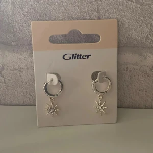 Örhängen - Snygga silverörhängen från Glitter med hängande stjärndetalj. Perfekta för att ge en glittrig touch till din outfit. Passar både till vardag och fest. Oanvända!