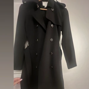 Svart trenchcoat - Elegant trench coat som är till knäna för mig som är 160. Samma kappa finns publicerad i annan artikel. Perfekt nu till hösten. Använd endast en gång 