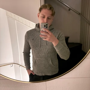 Grå hoodie från Polo Ralph Lauren - Säljer en gråmelerad hoodie från Polo Ralph Lauren med broderad logga på bröstet. Tröjan har huva med snörning, känguruficka och är tillverkad i ett stickat material. Perfekt för dig som gillar en clean och stilren look. Sitter mer som S