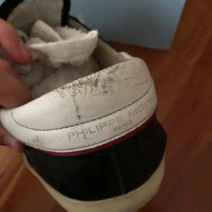 Svarta Philippe Model sneakers i skinn - Snygga svarta sneakers från Philippe Model Paris med vita detaljer och beige snörning. Skorna har en klassisk låg profil, vit sula och röd kant vid hälen. Tillverkade i skinn med rund tå och diskret logga på sidan. Perfekta för en trendig streetstyle-look. Och gick upp på höger skorn så limmade lite men syns inte så mycket men man kan slippa till det med slippapper 