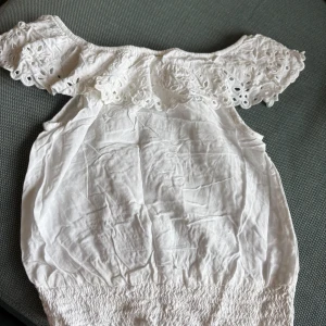 Vit topp - Superfin vit offshoulder topp med bred spetsvolang runt axlarna och smockad nederkant. Perfekt för dig som gillar romantisk och luftig stil. Tunn och lätt i bomull, perfekt till varma dagar.