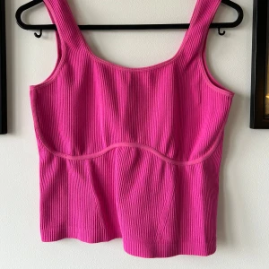 Ribbad rosa linnetopp - Snygg ribbad linnetopp i stark rosa färg med breda axelband och markerade sömmar under bysten. Toppen har en lite croppad passform men går ner till midjan på mig som är 173.