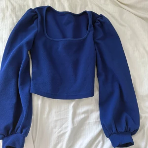 Blå croppad topp med puffärmar - Snygg blå croppad topp med fyrkantig urringning och långa puffärmar. Tjockare material som ger struktur och volym till ärmarna. Perfekt för dig som vill sticka ut med en trendig och färgstark look.