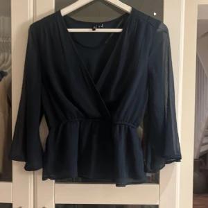 Mörkblå blus från Vero Moda - Säljer en mörkblå omlottblus från Vero Moda i storlek XS. Blusen har v-ringning, markerad midja och vida, transparenta ärmar i trekvarts längd. Tunt och lätt material som ger ett flowy intryck. Perfekt för dig som gillar stilrena och feminina detaljer.