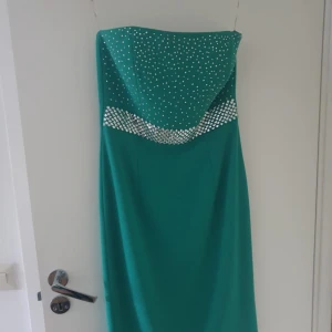 Grön axelbandslös klänning - Snygg grön axelbandslös klänning med glittriga silverdetaljer upptill. Klänningen har en elegant och figurnära passform, perfekt för speciella tillfällen. Utsmyckad med små och stora paljetter som ger en lyxig känsla.