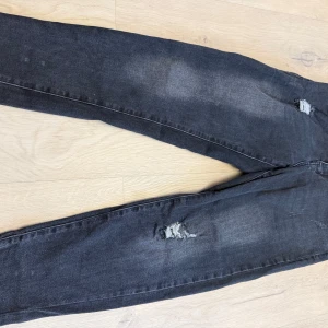 Svarta skinny jeans med slitningar - Säljer ett par svarta skinny jeans med snygga slitningar på benen. Jeansen har en tight passform och är tillverkade i stretchigt denimtyg för extra komfort. Perfekta för dig som gillar en lite tuffare stil.