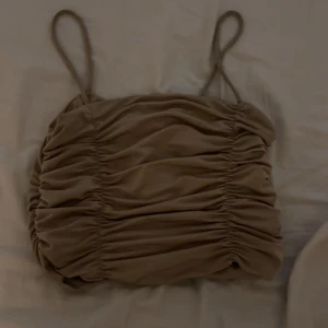 Beige topp med smala band - Säljer en beige topp med smala axelband och snygga rynkade detaljer över hela toppen. Modellen är croppad och har en cool, trendig look som passar perfekt till jeans eller kjol. Mycket skön och snygg men säljer då jag tyvärr växt ur den. Lappar är bortklippta men har för mig den kommer från SHEIN. 