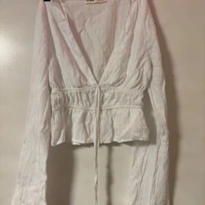 Vit omlottopp från Pull&Bear XS - Säljer en vit omlottopp från Pull&Bear i storlek XS. Toppen har långa ärmar, v-ringning och knytband i midjan. Skit snygg och sexig passar jätte bra för sommaren