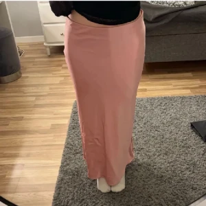 Rosa långkjol i satin från Zara - Supersnygg rosa långkjol från Zara i glansigt satinmaterial. Kjolen har en rak och slimmad passform som sitter tajt över höfterna och faller snyggt ner till anklarna. Använd fåtal gånger💕