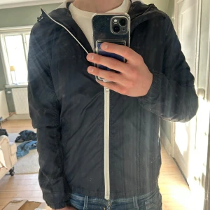 Blå vindjacka från Tom tailor - Säljer en blå vindjacka med vit dragkedja och huva. Jackan har långa ärmar och en enkel design som passar perfekt för vår och höst. Personen på bilden är ca 180 cm lång och väger 70 kg. Tveka inte på att kontakta mig vid minsta fundering eller eventuella frågor🙌