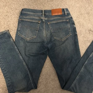 Blå jeans från Tiger of Sweden - Snygga blå jeans från Tiger of Sweden med klassisk femficksdesign och knappgylf. Tillverkade i Italien, dessa jeans har en stilren look och är perfekta för en avslappnad stil. Märkeslappen i läder ger en extra touch av kvalitet.