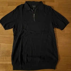 Marinblå pikétröja från H&M - Snygg marinblå pikétröja från H&M med dragkedja framtill. Perfekt för en stilren look. Tröjan har korta ärmar och en klassisk krage.