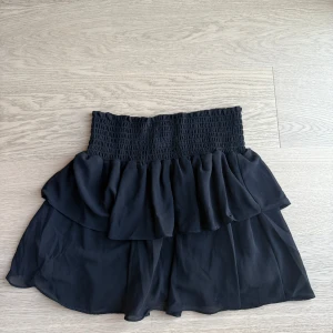 Svart kortkjol med volang - Snygg svart kortkjol med volangdetaljer och elastisk midja.