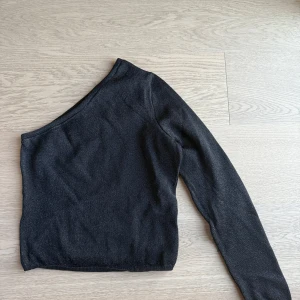 Svart oneshoulder topp - Snygg svart oneshoulder topp med lång ärm.  Materialet är mjukt, bekvämt och skimrigt. 