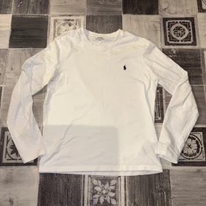 Vit långärmad tröja från Polo Ralph Lauren - Säljer en klassisk vit långärmad tröja från Polo Ralph Lauren. Tröjan har en liten broderad logotyp på bröstet och är tillverkad i mjuk bomull. Perfekt för en stilren och avslappnad look.