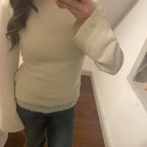 Vit stickad tröja - Säljer en stilren vit stickad tröja med långa ärmar och ribbade detaljer vid ärmslut och nederkant. Perfekt för kyligare dagar och lätt att matcha med olika outfits.