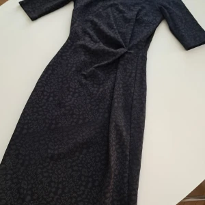 Svart klänning från Ilse Jacobsen - Snygg svart klänning från Ilse Jacobsen i storlek XS. Klänningen har ett diskret leopardmönster och en knytdetalj framtill. Tillverkad i polyester och elastan för en bekväm passform. Den är svart grå i färgen. Inte helt svart. 