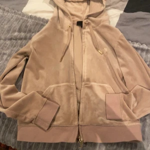Beige hoodie från Juicy Couture - Säljer en beige hoodie från Juicy Couture med dragkedja och huva. Den har långa ärmar och snörning i huvan med gulddetaljer. Perfekt för en avslappnad stil. Anledning till varför jag säljer den är för jag inte tycker om färgen. 