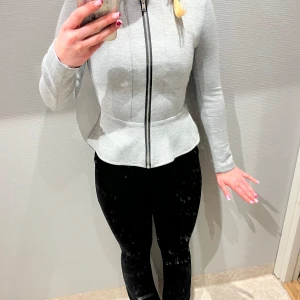 Grå zip-up tröja - Säljer en stilren grå zip-up tröja med lång ärm och dragkedja framtill. Tröjan har en figurnära passform och en lätt utsvängd nederkant. Perfekt för en casual look eller lager på lager-stil.