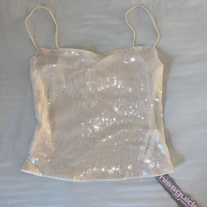 Beige paljettopp från Missguided - Säljer en glittrig beige paljettopp från Missguided med tunna axelband. Perfekt för en kväll ute eller festliga tillfällen! Aldrig använd så lapparna sitter kvar. Lite lätt genomskinlig vilket jag tycker är supersnyggt! 🦋🩵