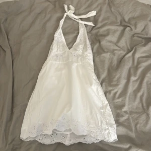 Vit klänning från Zara - Säljer en söt vit klänning från Zara med knytband i nacken och v-ringad design. Klänningen har broderade detaljer och en kort längd, perfekt för varma dagar. Den är tillverkad i ett lätt och luftigt material. Buda gärna! Blir det en affär så sker det genom Swish och jag kommer skicka bild och video bevis när jag skickar klänningen till dig som köper den.❤️