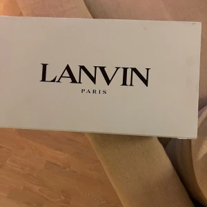 Svarta sneakers från Lanvin - Snygga svarta sneakers från Lanvin med glansiga detaljer på tån och snörning. Skorna har en klassisk design med en vit sula som ger en stilren kontrast. Perfekta för en trendiga stilen, skriv direkt vid frågor, priset är ej hugget i sten. Liten defekt i skon.