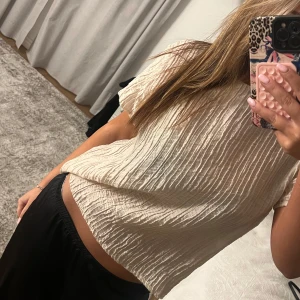 Beige ribbad blus - Säljer en stilren beige blus med ribbad textur. Blusen har korta ärmar och en lös passform. Endast använd en gång